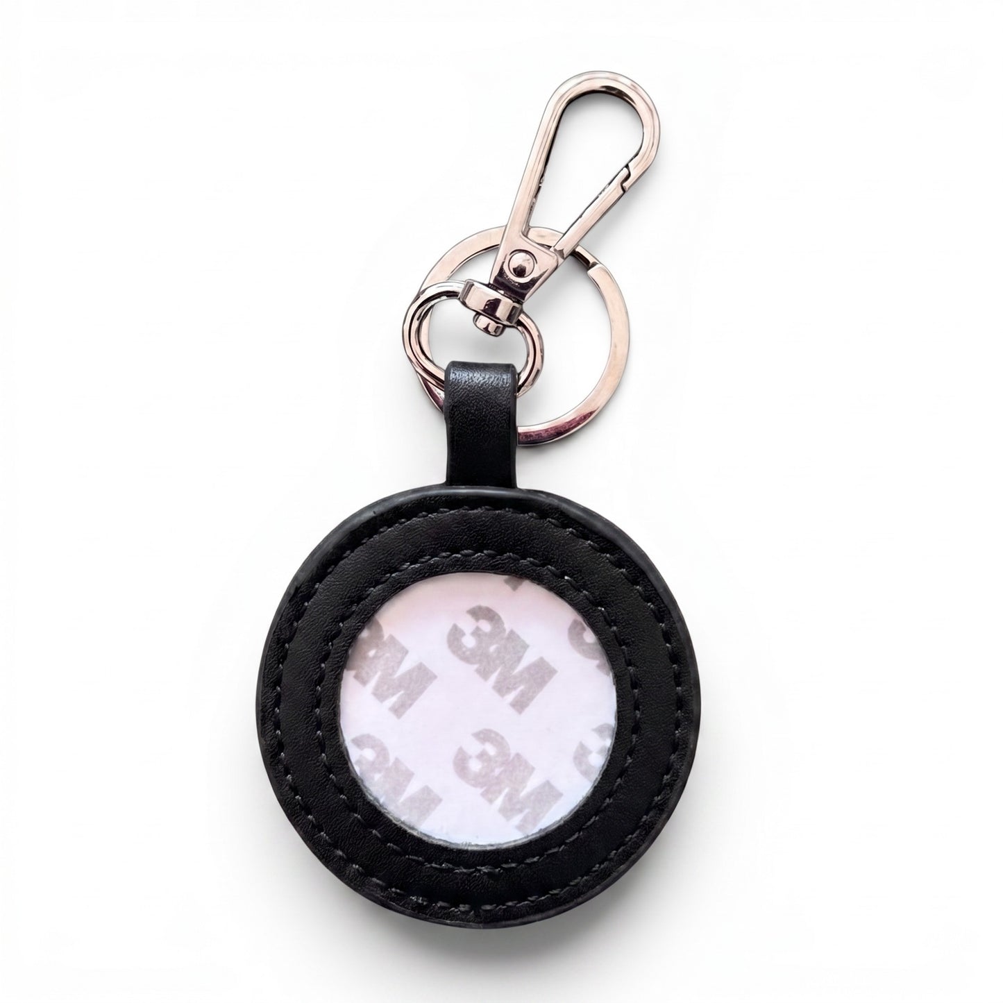 A circular black faux-leather keychain holder with a clear window showing a white 3M adhesive backing, attached to a rose gold split ring and carabiner clip on a white background.