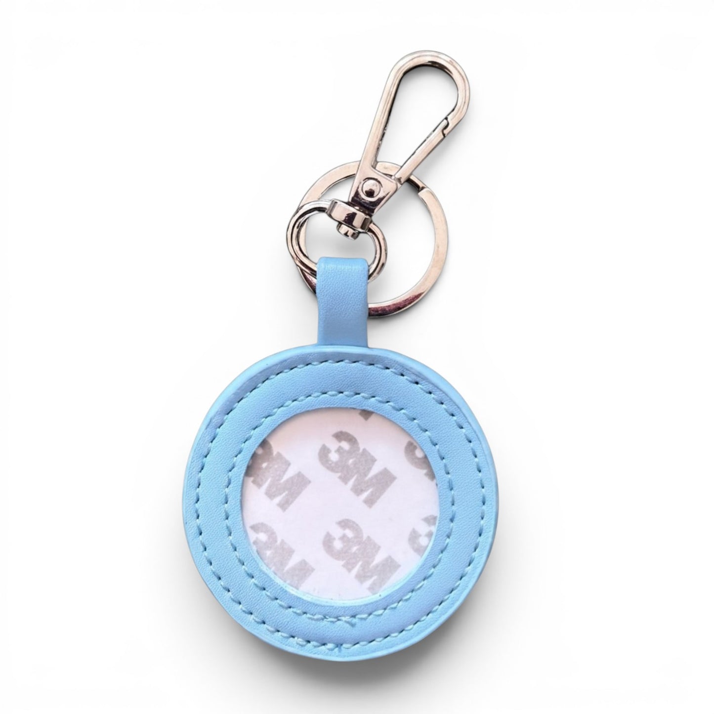 A light blue circular keychain holder with a silver metal clasp and key ring, shown on a clean white background. The inside of the holder reveals a white 3M adhesive backing.