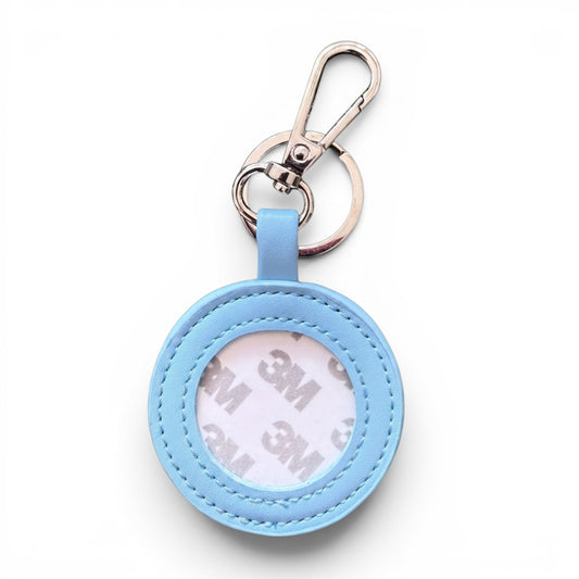 A light blue circular keychain holder with a silver metal clasp and key ring, shown on a clean white background. The inside of the holder reveals a white 3M adhesive backing.